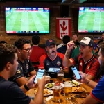 Engaged bettors reviewing kèo nhà cái in a lively sports bar during a football match.